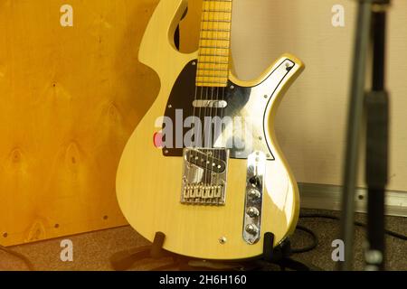 Una chitarra elettrica gialla si trova contro un muro in uno studio musicale professionale. Strumento musicale firmato a corde di colore brillante. Acustica perfetta Foto Stock