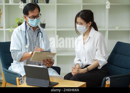 Un medico di sesso maschile di età professionale richiede informazioni sui sintomi di una paziente femminile e prende le note mediche. Foto Stock