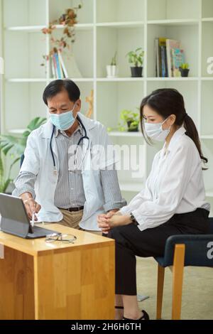 Un terapista di sesso maschile anziano parla e diagnostica la malattia con una paziente femminile. Un medico e un paziente discutono delle opzioni di trattamento. Foto Stock