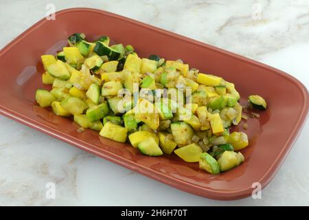 Zucchine tritate saltate e zucca estiva gialla al crookneck e contorno di verdure allo scalogno su piatto di portata rosso Foto Stock