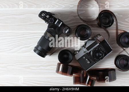 Filma vecchie macchine fotografiche con obiettivi e film manifestati su uno sfondo bianco di legno con spazio di copia. Foto Stock