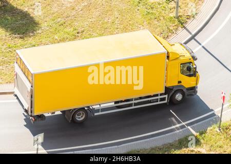 Il carrello giallo con contenitore isolato gira sull'autostrada, vista aerea Foto Stock