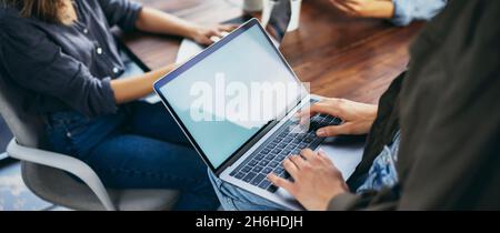 Immagine mockup di una donna che utilizza un computer portatile con schermo vuoto su un tavolo di legno. Tastiera a mani femminili sul computer Foto Stock