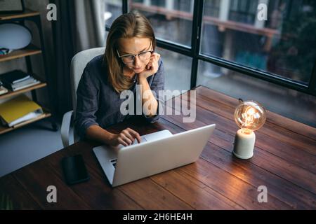 Giovane donna che lavora con un notebook. Freelance femminile che si connette a internet via computer. Blogger o giornalista che scrive nuovo articolo. Foto Stock