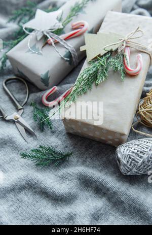 Scatole regalo decorative natalizie fatte in casa avvolte in carta kraft marrone su sfondo di maglia tessile grigio Foto Stock