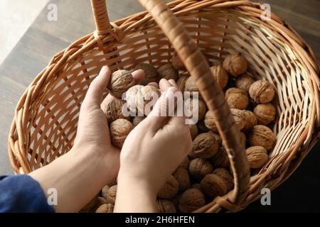 Mani femminili che tengono noci sullo sfondo di un cesto di noci. Mani di donna che tengono noci fresche sopra un cesto pieno di noci Foto Stock