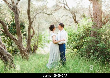 Kotor, Montenegro - 21.06.17: Uomo sorridente che abbraccia la donna in vita mentre si trova in erba tra verde uliveto Foto Stock