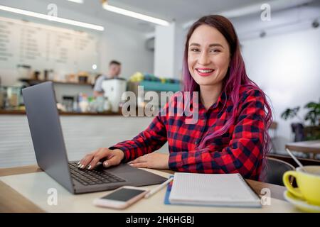 Giovane donna con capelli rosa con computer portatile in seduta cafe, intelligente studentessa lavorando su net-libro. Foto Stock