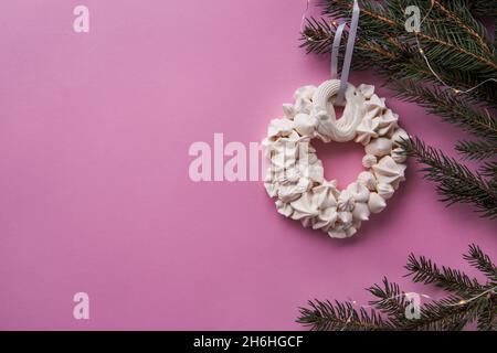 Corona meringa di Natale sul ramo di abete sullo sfondo di colore rosa. Concetto di scheda. Vista dall'alto. Disposizione piatta Foto Stock