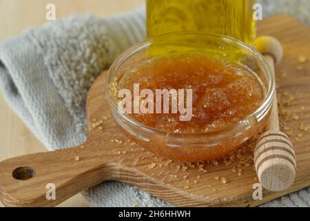 Scrub alle labbra fatto in casa con zucchero di canna, miele e olio d'oliva in una ciotola di vetro su un tagliere di legno - prodotto di bellezza naturale Foto Stock