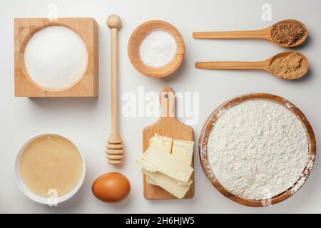 Ingredienti per la cottura di biscotti di zenzero di Natale in ciotole di legno su tavola bianca. Knolling. Miele, zucchero, soda, zenzero, cannella, burro, uovo, fiu Foto Stock