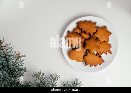 Biscotti di pan di zenzero di Natale a forma di stelle e alberi in piatto bianco con rami di albero di Natale. Vista dall'alto. Spazio di copia Foto Stock