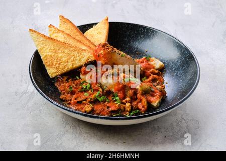 Zander fritto servito con pomodoro al vapore, cipolla e salsa di olive su un piatto Foto Stock