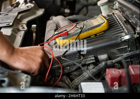 Il meccanico automatico misura la tensione con un multimetro. Foto Stock