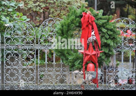 Decorazioni invernali in giardino. Una corona di abeti natalizi con arco rosso, stella e campana su un cancello da giardino metallico Foto Stock