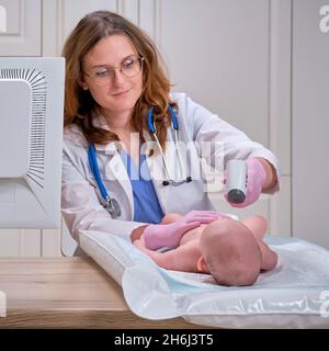 Il medico controlla la temperatura del neonato con un termometro. Un infermiere in uniforme misura la febbre del bambino con un termometro Foto Stock