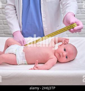 Il medico misura la crescita di un neonato. Un infermiere in uniforme controlla la circonferenza della testa e dell'addome del bambino Foto Stock