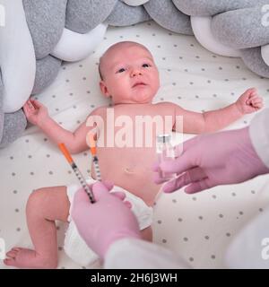 Il medico usa una siringa per iniettare un neonato. Un'infermiera in uniforme si prepara a vaccinare un bambino Foto Stock