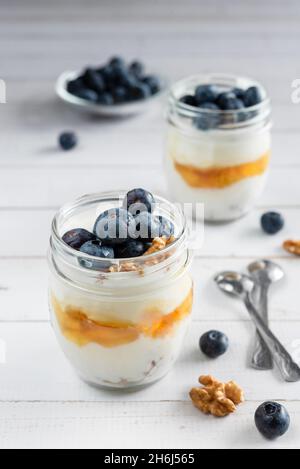 Yogurt greco naturale con mirtilli freschi e miele in un vaso. Mangiare sano. Scatto verticale Foto Stock