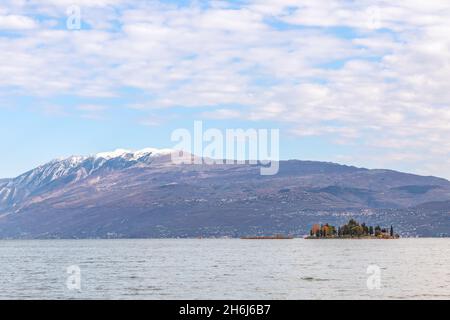 Piccola isola di coniglio sul Lago di Garda sullo sfondo delle Alpi (periodo autunnale) Foto Stock