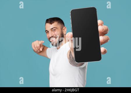 Sorridente ragazzo europeo mostrare dito al telefono con schermo vuoto e consiglia gadget Foto Stock