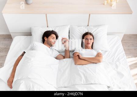 Deluso sconvolto caucasica giovane signora sveglio, sdraiato a letto, signora che soffre di rumore e apnea, marito dormire Foto Stock