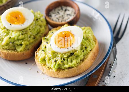 Buon toast avocado con uova sode e semi di sesamo sul piatto, vista closeup Foto Stock
