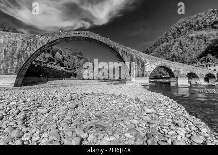 Antico Ponte della Maddalena o Ponte del Diavolo in bianco e nero, sotto un cielo drammatico, Borgo a Mozzano, Lucca, Italia Foto Stock