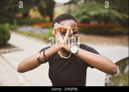 Primo piano ritratto di attraente felice sorridente giovane bellezza naturale capelli corti donna africana che indossa nero t-shirt ridere allungando le mani di chiusura dalla macchina fotografica nel parco naturale estivo Foto Stock