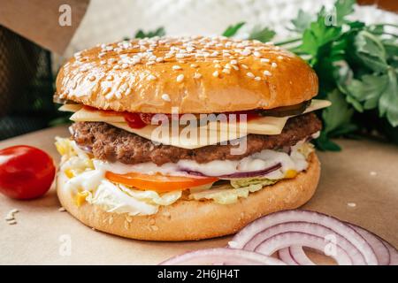 Doppio hamburger classico con cotoletta di carne, lattuga, pomodoro, cetriolo sottaceto, formaggio, cipolla e salsa su carta artigianale con pomodori ciliegini e parsl verde Foto Stock