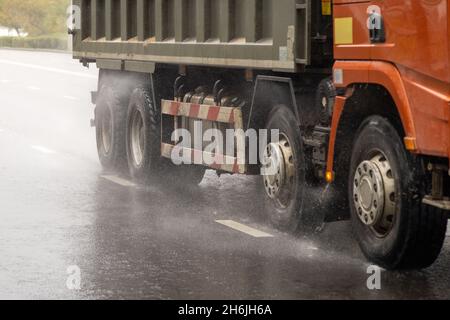 autocarro pesante in movimento su strada bagnata con spruzzi durante il giorno Foto Stock