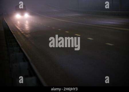 minivan da solo in movimento su una strada vuota e piena di nebbia notturna Foto Stock