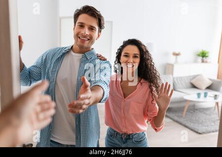 Felice giovane coppia che invita la gente ad entrare a casa, scuotendo le mani Foto Stock