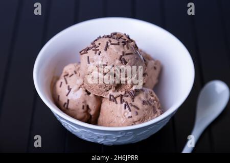 Gelato al cioccolato con cioccolato spruzzare in una ciotola bianca su fondo nero. Tre palle di gelato fatto in casa. Primo piano. Foto Stock