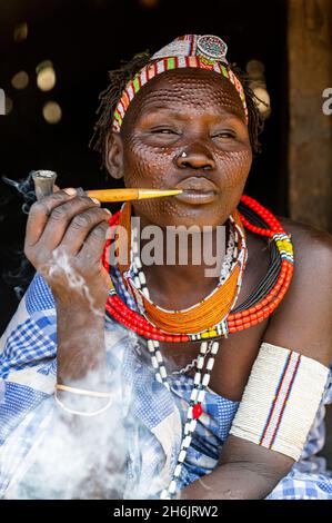 Donna con cicatrici di bellezza della tribù Toposa che fuma una pipa, Equatoria orientale, Sudan del Sud, Africa Foto Stock