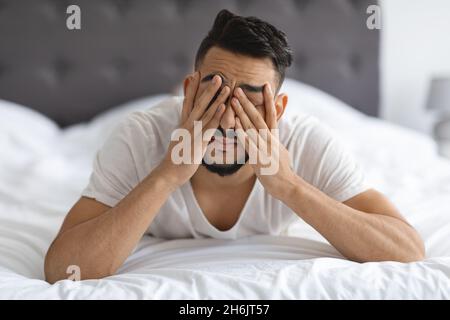 Giovane uomo arabo che si sveglia a letto, strofinando gli occhi dopo la notte insonne Foto Stock