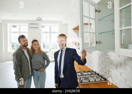 Agente immobiliare che mostra buyers cucina armadi mentre dando giro circa casa nuova Foto Stock