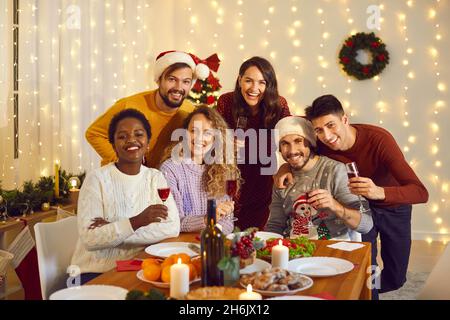 Ritratto di gruppo di amici allegri e diversi al tavolo delle feste al party di Natale a casa Foto Stock