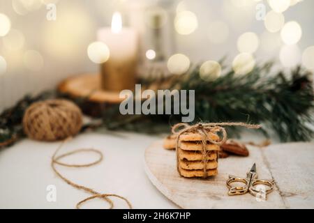 Accogliente atmosfera natalizia. Biscotti artigianali a forma di albero di Natale in vassoio di legno sul tavolo con ramo di abete e candele Foto Stock
