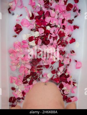 L'uomo prende un bagno con latte e petali di rosa. Foto Stock