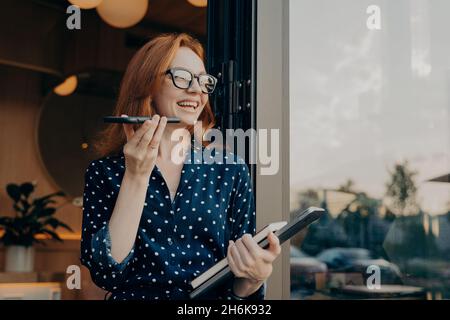 Donna con capelli rossi tiene le conversazioni telefoniche con l'altoparlante con gli amici fa il riconoscimento vocale Foto Stock