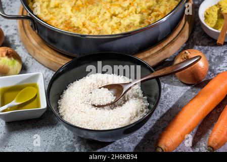 Risotto vegano italiano in padella grande con ingredienti - riso, cipolla, carote, spezie, olio d'oliva Foto Stock