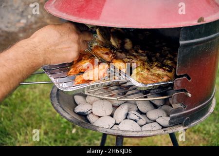 primo piano della mano di un uomo anziano che gira la carne sul grill Foto Stock