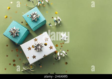 Scatole regalo bianche e verdi con un tinsel e confetti su sfondo verde. Il concetto di un regalo, un nuovo anno, un background festivo. Disposizione piatta, vista dall'alto Foto Stock