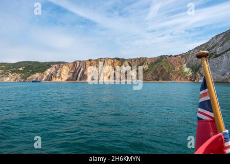 Barche ormeggiate nella baia di allume con le sue scogliere di sabbia multicolore con bandiera inglese rossa sul flagestaff in primo piano, Isola di Wright Hampshire Foto Stock