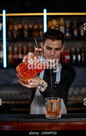 il barman in grembiule versa un cocktail vecchio stile in un bicchiere Foto Stock