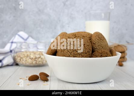 Biscotti di farina d'avena in un recipiente bianco e un bicchiere di latte su sfondo concreto Foto Stock