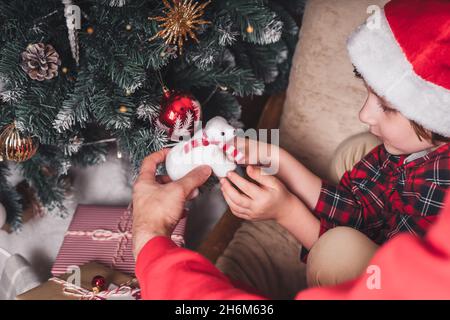 Primo piano delle mani del padre e del bambino appesi il giocattolo decorativo sul ramo dell'albero di Natale Foto Stock