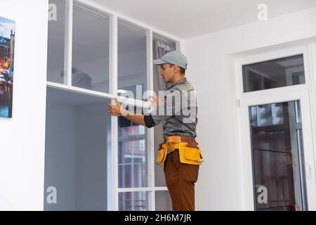 Lavoratore di costruzione che installa il profilo di metallo per la parete interna di divisorio, mentre costruisce una nuova casa o processo di rinnovamento, visto dalla sua parte posteriore. Foto Stock