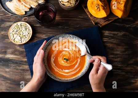 Le mani femminili raccolgono la zuppa di crema di zucca con un cucchiaio, cibo vegetariano sano, vista dall'alto. Foto Stock